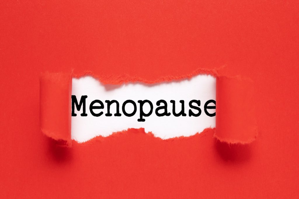 Word Menopause written on white background, view through hole in red paper